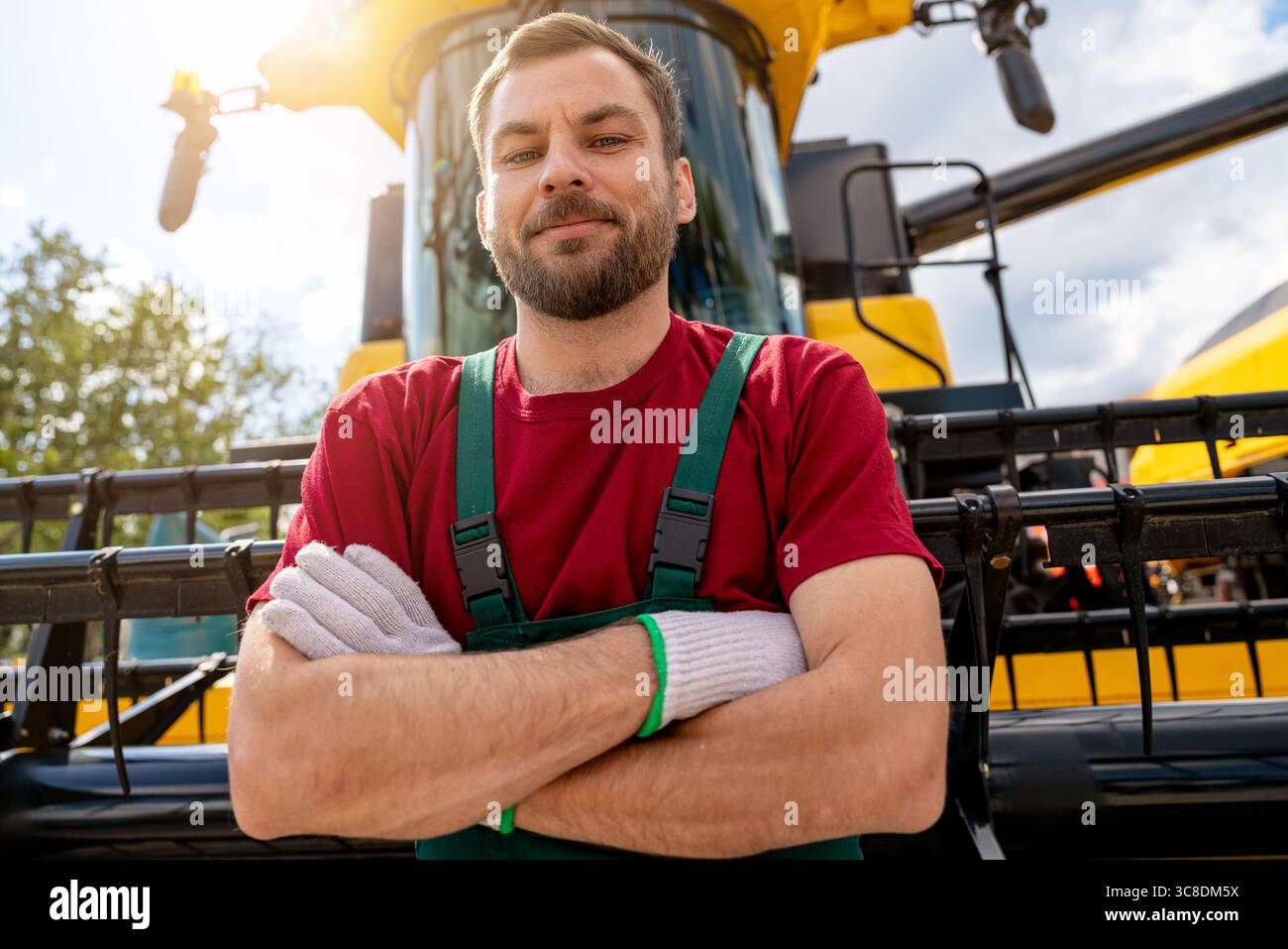 Portrait de l'opérateur de machines agricoles debout en toute confiance devant la moissonneuse-batteuse Banque D'Images