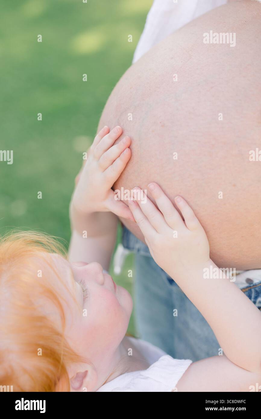 L'enfant touche le ventre enceinte avec les deux mains à l'extérieur. Banque D'Images