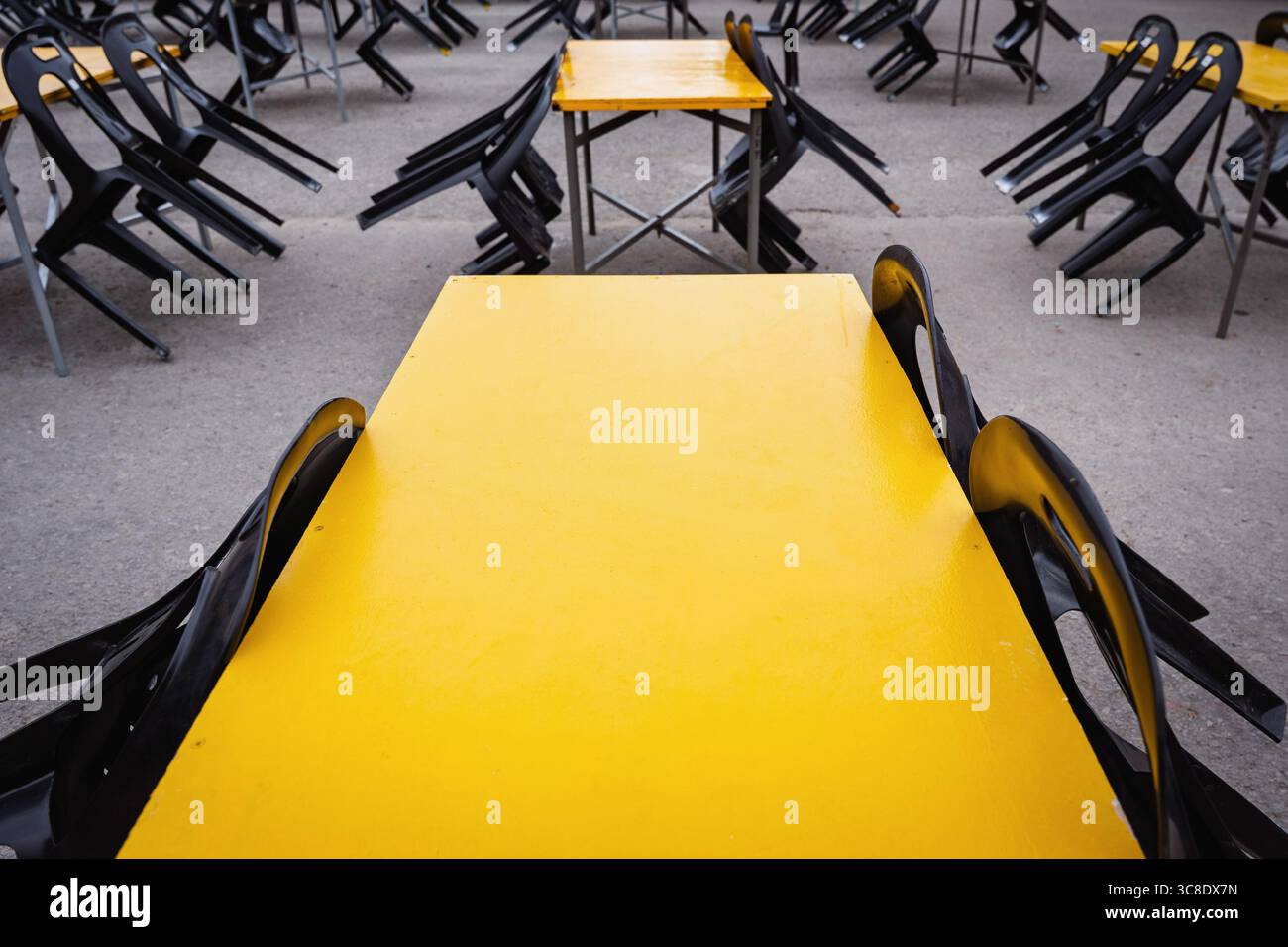 Salle à manger extérieure vide avec tables jaunes et chaises noires inversées. Banque D'Images