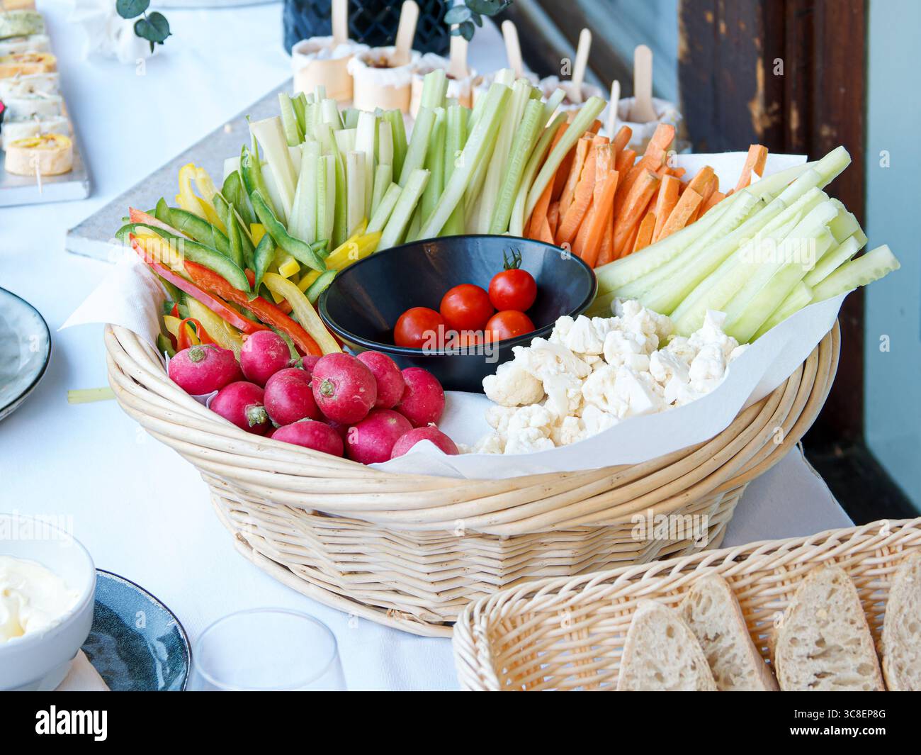 Panier en osier rempli d'un assortiment de légumes crus frais comprenant radis, poivrons, concombre, carottes, tomates cerises et chou-fleur, Banque D'Images