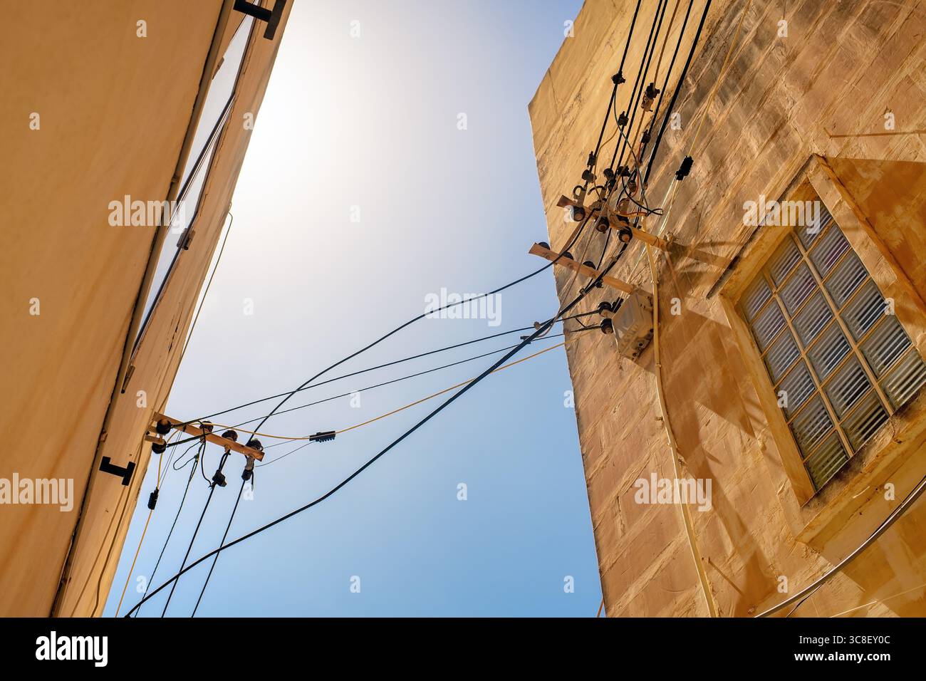 Vue en angle bas des câbles électriques avec isolateurs en céramique, pinces en plastique, joints de fil et supports de montage entre façades en pierre contre le ciel. Banque D'Images