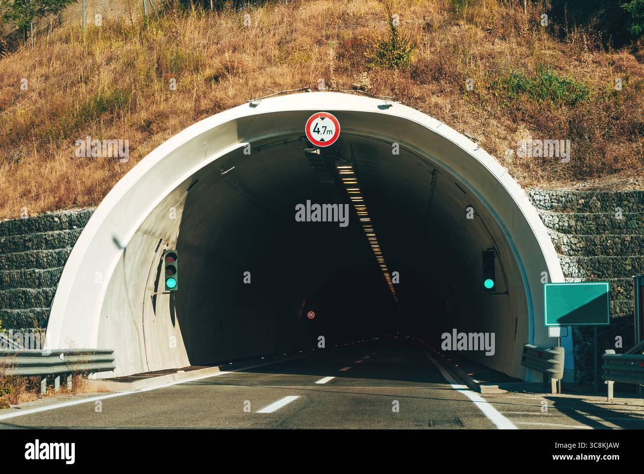 Entrée de tunnel routier moderne dans une région montagneuse sèche avec des feux verts et un panneau de limite de hauteur. Mise au point sélective. Banque D'Images