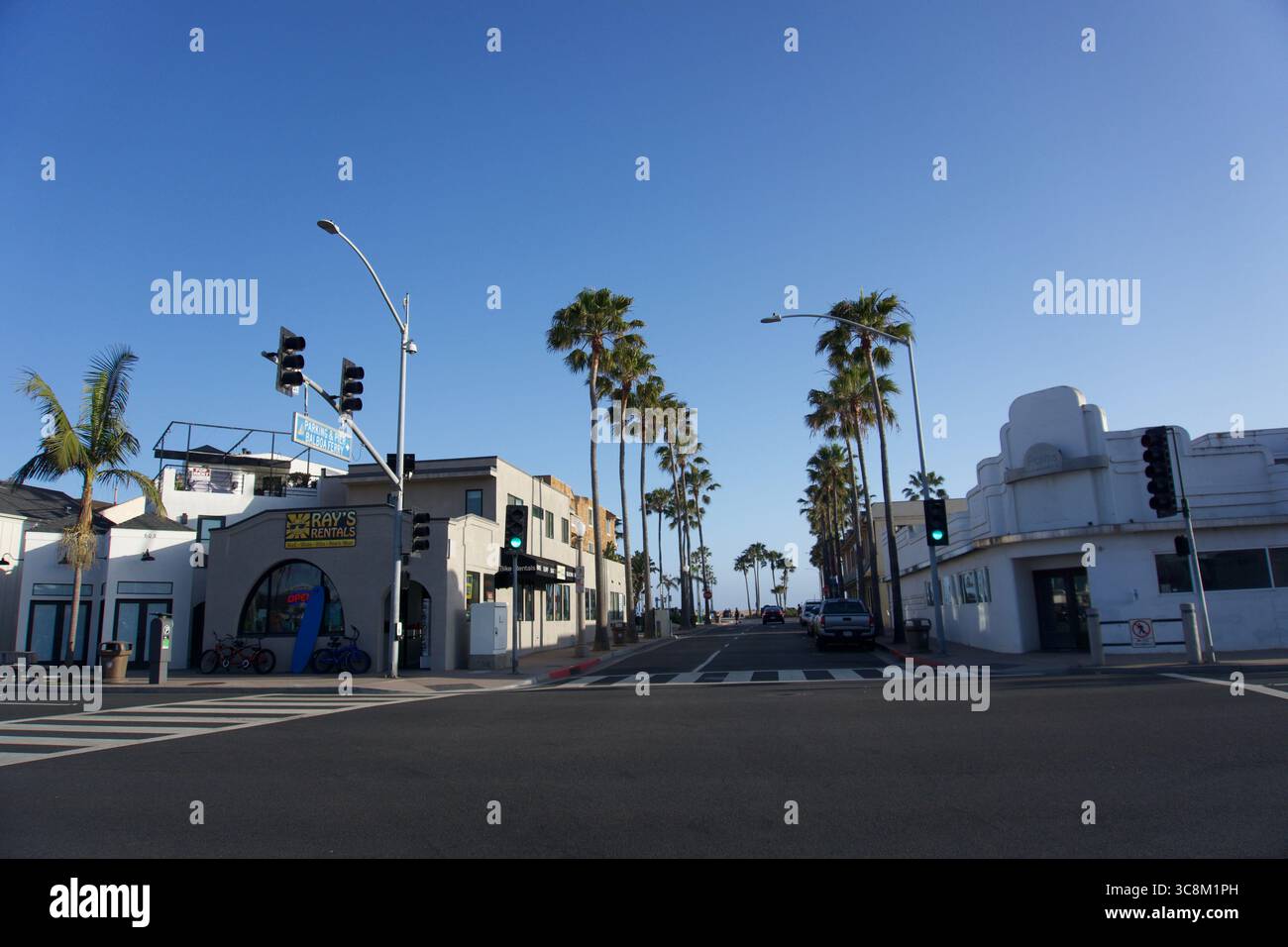 Une rue calme bordée de palmiers à Newport Beach mène directement à l'océan sous un ciel bleu clair, avec des magasins locaux et le charme côtier en vue Banque D'Images