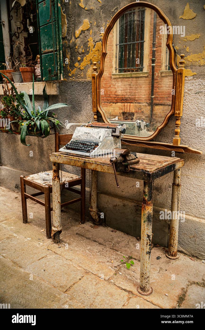 Machine à écrire vintage et chaise en bois à l'extérieur d'un bâtiment rustique dans une ruelle vénitienne, Italie. Banque D'Images