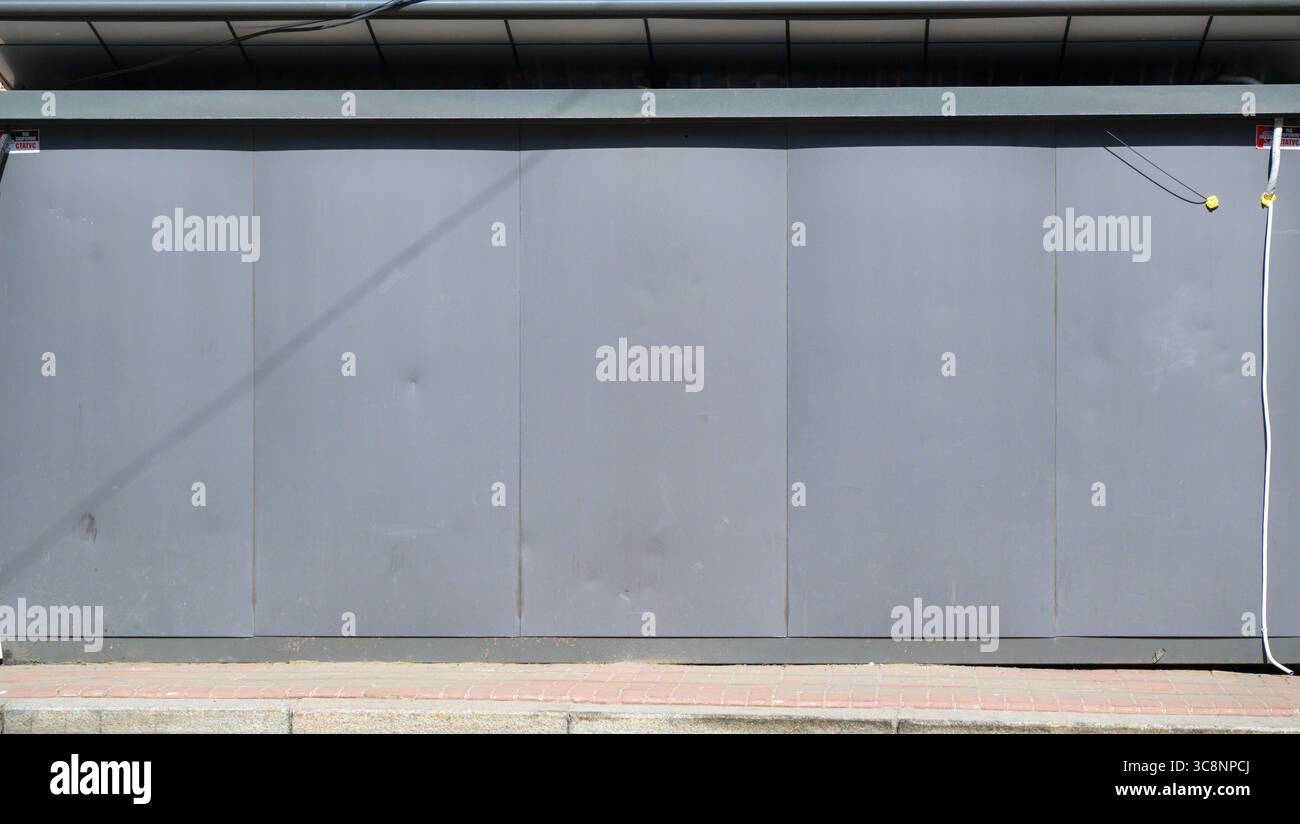 Les volets de vitrine en métal gris sont complètement fermés, protégeant une entreprise, avec des fils électriques suspendus sur le côté droit et un trottoir de briques à l'intérieur Banque D'Images