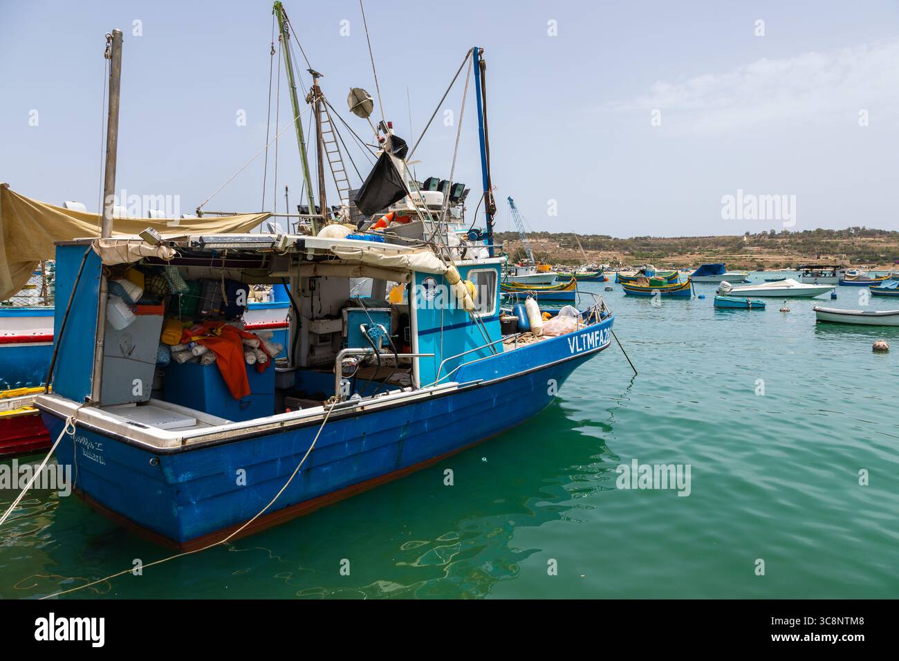 Marsaxlokk, Malte – 22 juin 2021 : bateau de pêche bleu amarré dans le port avec des bateaux traditionnels maltais en arrière-plan. Banque D'Images