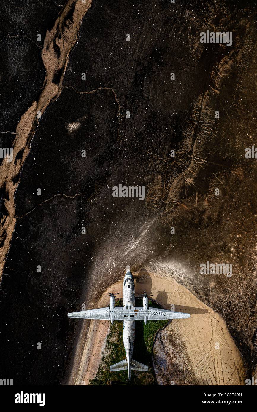 Vue aérienne d'un avion altéré reposant au milieu du contraste saisissant de la terre sombre et fissurée et de la lumière, chemins graveleux, créant un récit visuel saisissant, la Pologne. Banque D'Images