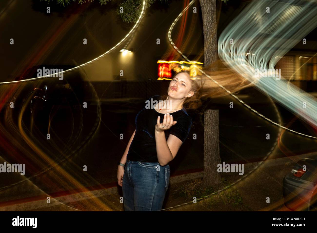 Une femme se tient gracieusement sous un lampadaire lumineux par une belle nuit, créant une atmosphère enchanteresse tout autour d'elle Banque D'Images