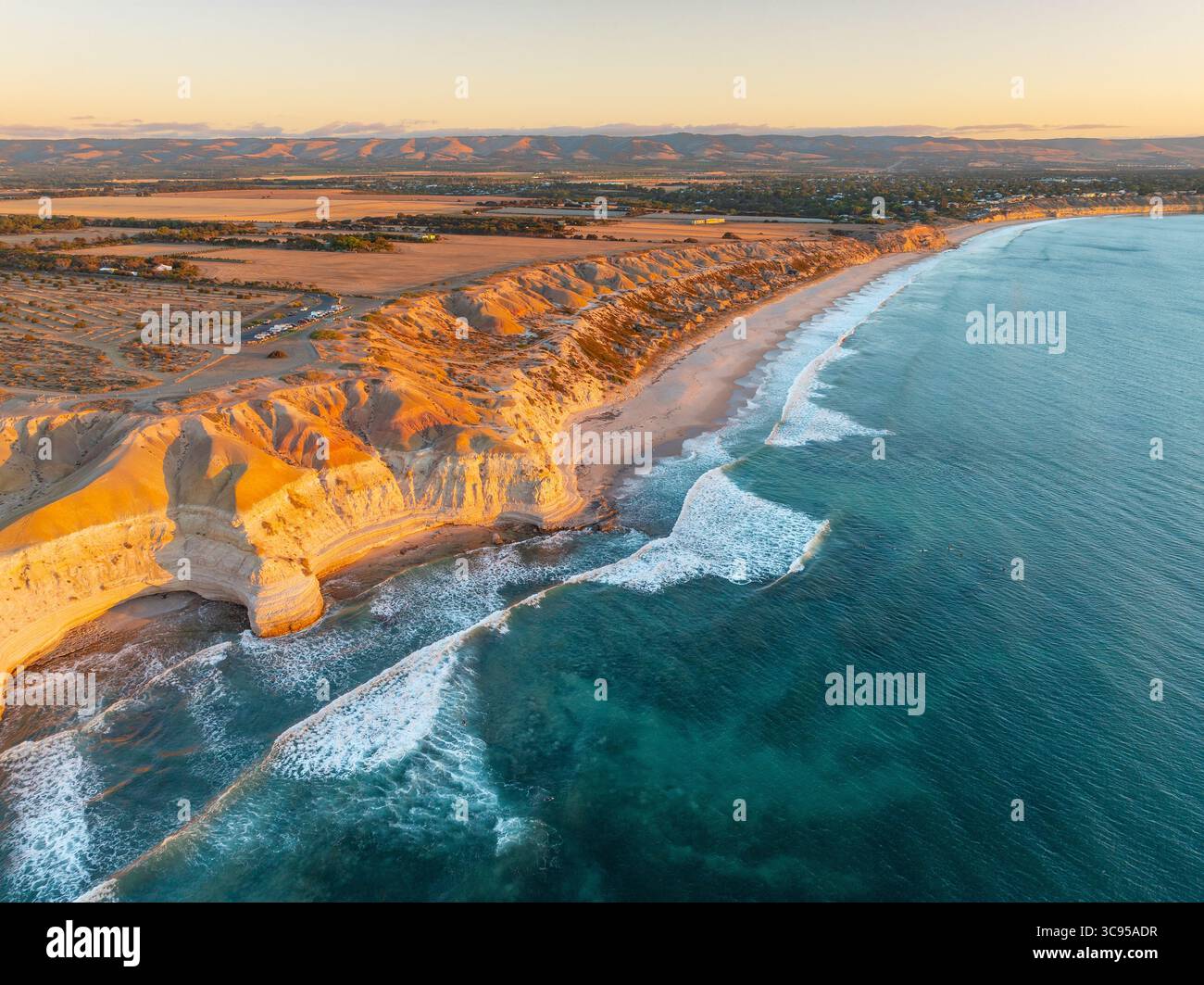Vue aérienne des vagues roulant sur une plage étroite sous une côte accidentée dans la lumière dorée à Maslin Beach sur la péninsule de Fluerieu en Australie méridionale Banque D'Images