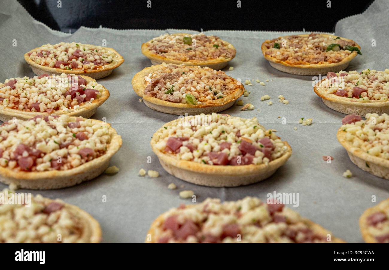 Un plateau de mini pizzas avec garnitures de fromage et de viande. Les pizzas sont disposées en rangée nette sur une plaque à pâtisserie Banque D'Images