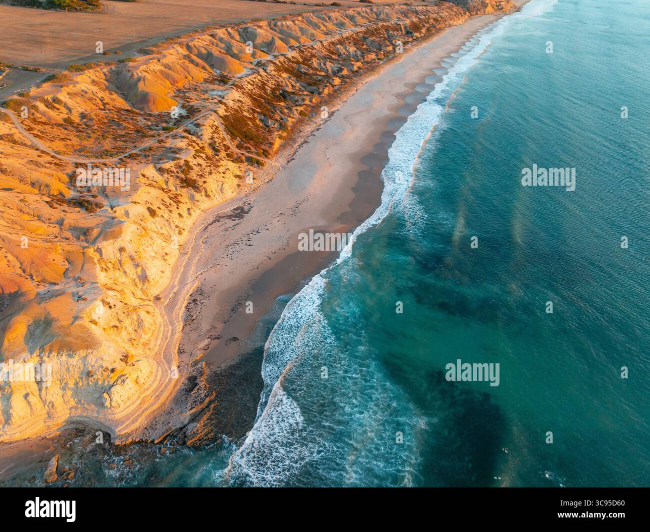 Vue aérienne des vagues roulant sur une plage étroite sous une côte accidentée dans la lumière dorée à Maslin Beach sur la péninsule de Fluerieu en Australie méridionale Banque D'Images