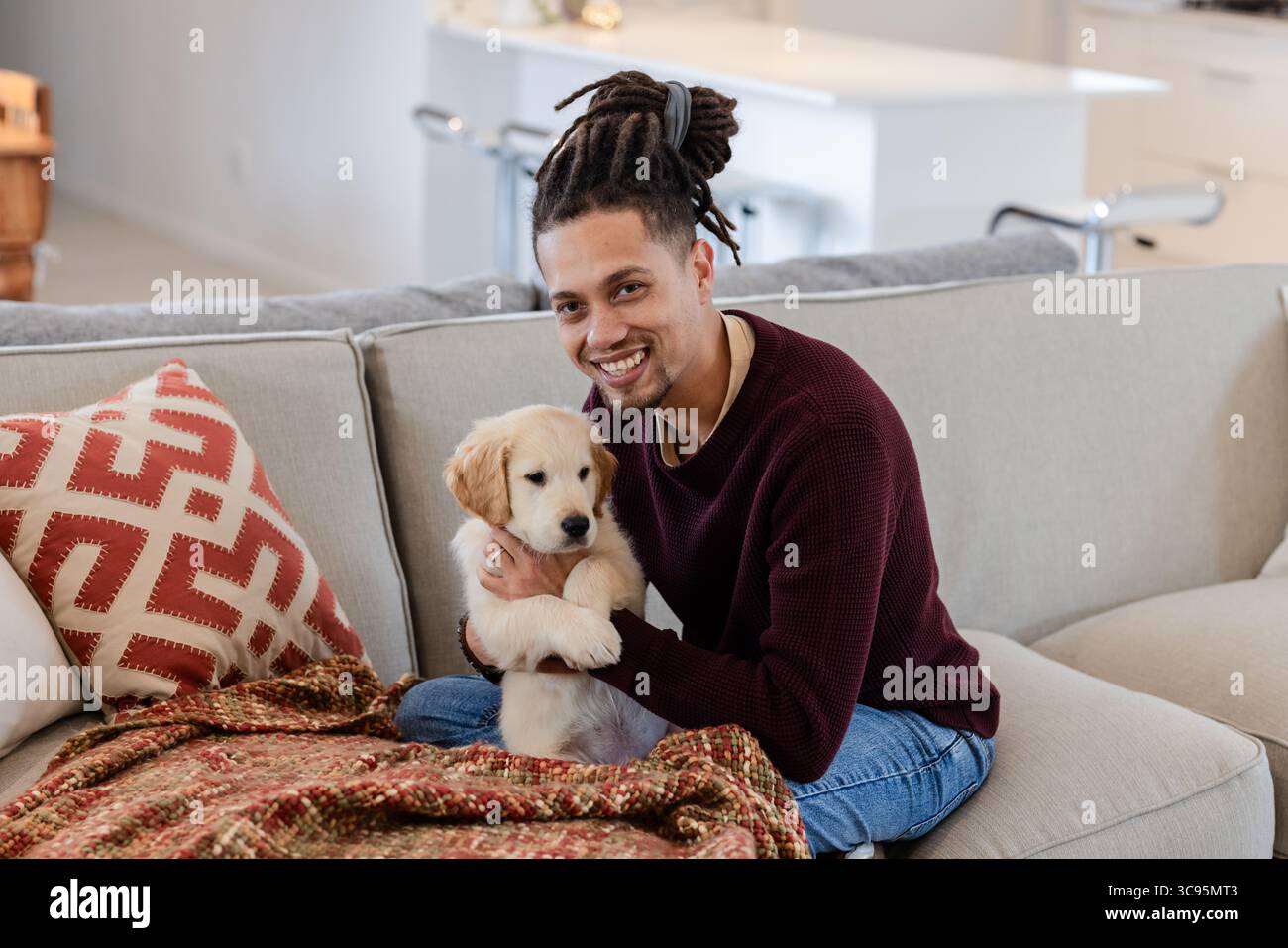 Homme afro-américain tenant le chiot Golden retriever tout en étant assis sur le canapé dans le salon ouvert Banque D'Images Homme afro-américain tenant le chiot Golden retriever tout en étant assis sur le canapé dans le salon ouvert Banque D'Images
