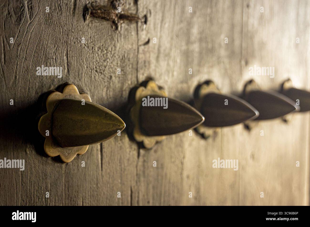 Vue de la porte en bois vieilli ornée de boutons en laiton ornés, leurs formes coniques attrapant la lumière dans une lueur chaude, Lamu, Kenya. Banque D'Images