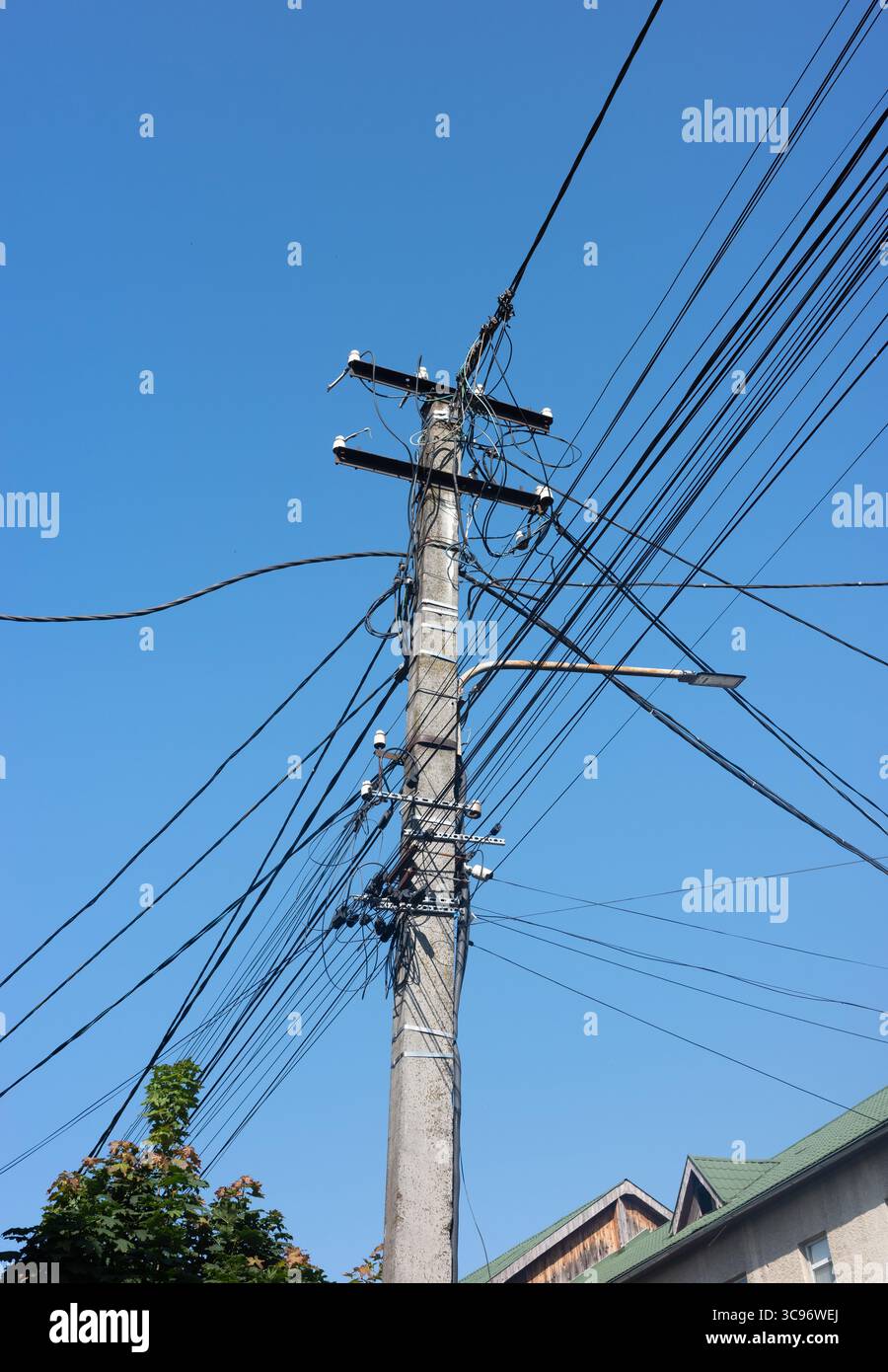 Un poteau électrique avec de nombreux fils contre un ciel bleu vif, avec un lampadaire et un bâtiment visibles. Banque D'Images