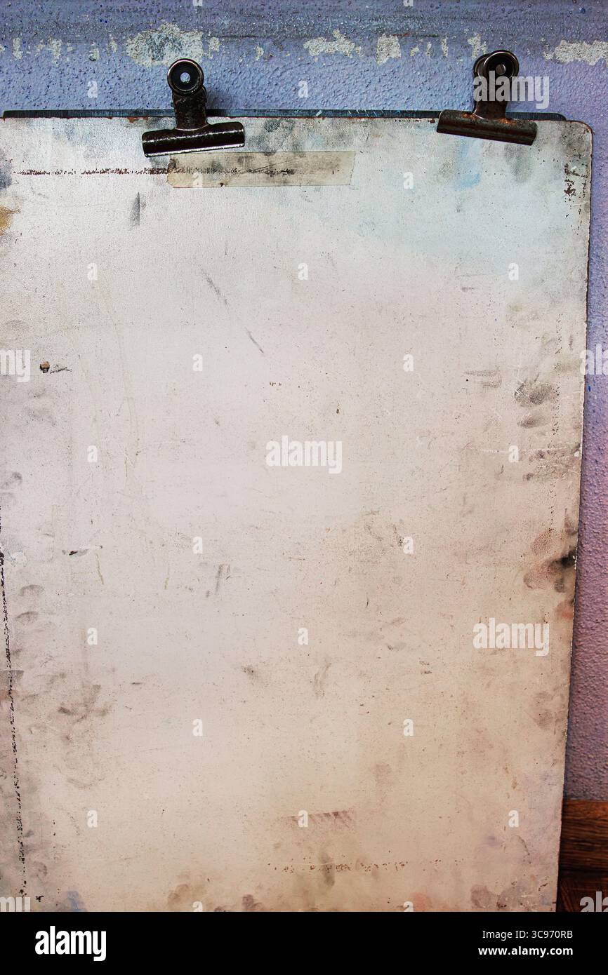 Vieille planche à dessin usée avec deux clips de reliure en métal rouillé, monté contre un mur texturé pastel délavé. Banque D'Images