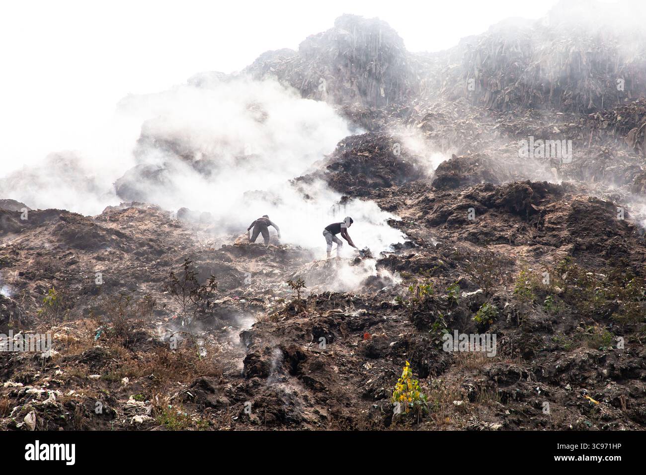 Chittagong, Bangladesh - 12 février 2024 : vue des travailleurs au milieu du paysage fumant et texturé d'une décharge, où dansent les bruits de fumée Banque D'Images