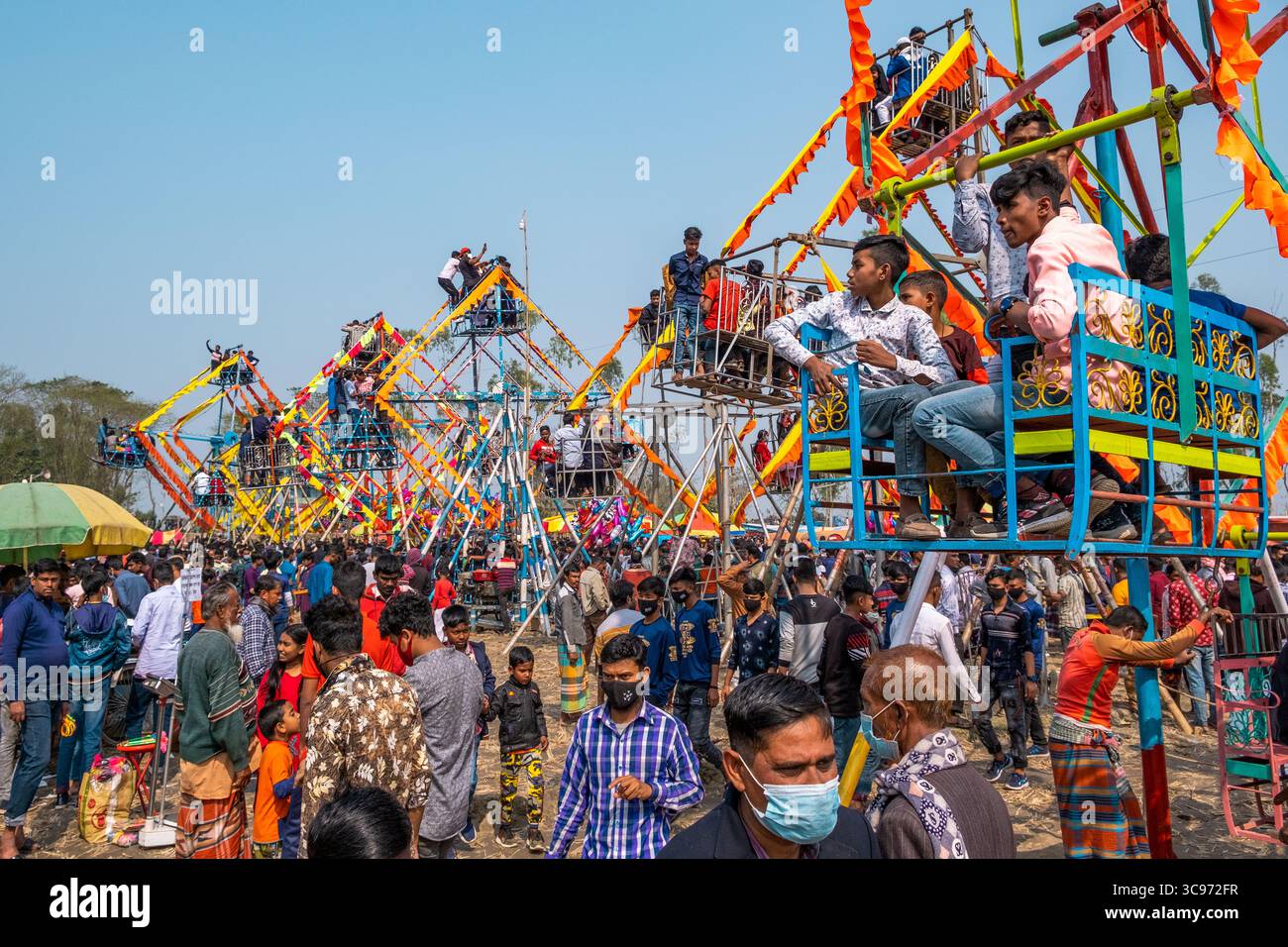 Bogura, Bangladesh - 03 novembre 2023 : vue sur une scène de foire vibrante, les grandes roues colorées dominant une foule dense sous un ciel clair. Banque D'Images
