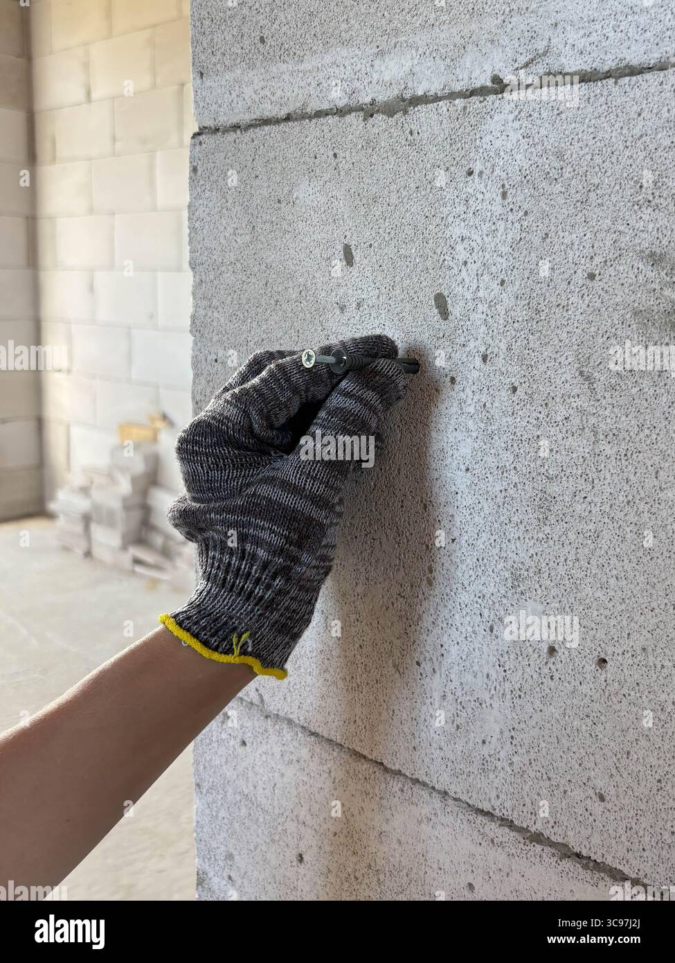 Une main dans un gant de protection tient un clou près d'un mur pour l'enfoncer. Chantier de construction. Rénovation, nouveau bâtiment. Banque D'Images