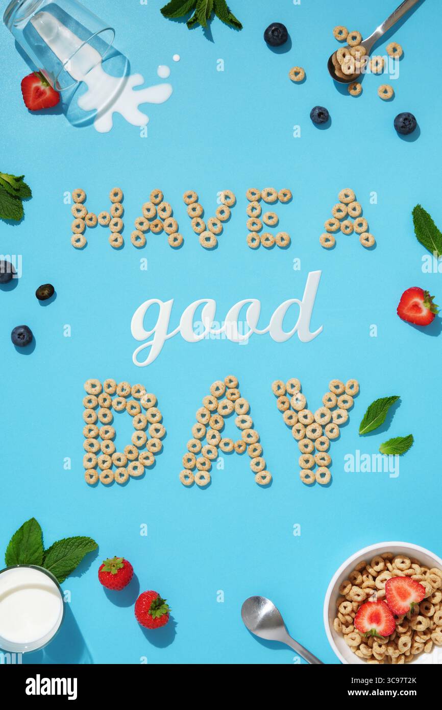 Les mots ont une bonne journée faite d'anneaux de céréales, de lait, de fraises, de bleuets et de feuilles de menthe sur un fond bleu. Idée de petit déjeuner positive. Banque D'Images