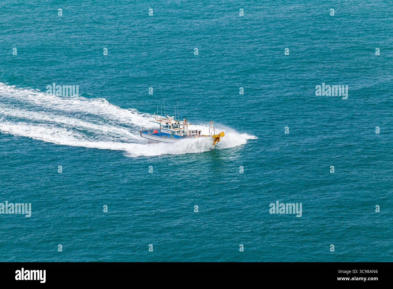 Un bateau de pêche coupe rapidement à travers les eaux bleu de l'océan, créant une traînée de mousse blanche. La scène vibrante capture l'activité maritime et le Banque D'Images
