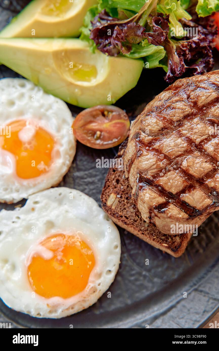 Une assiette délicieusement préparée avec steak grillé, œufs frits, salade fraîche et tranches d'avocat, parfait pour un copieux petit déjeuner ou déjeuner Banque D'Images
