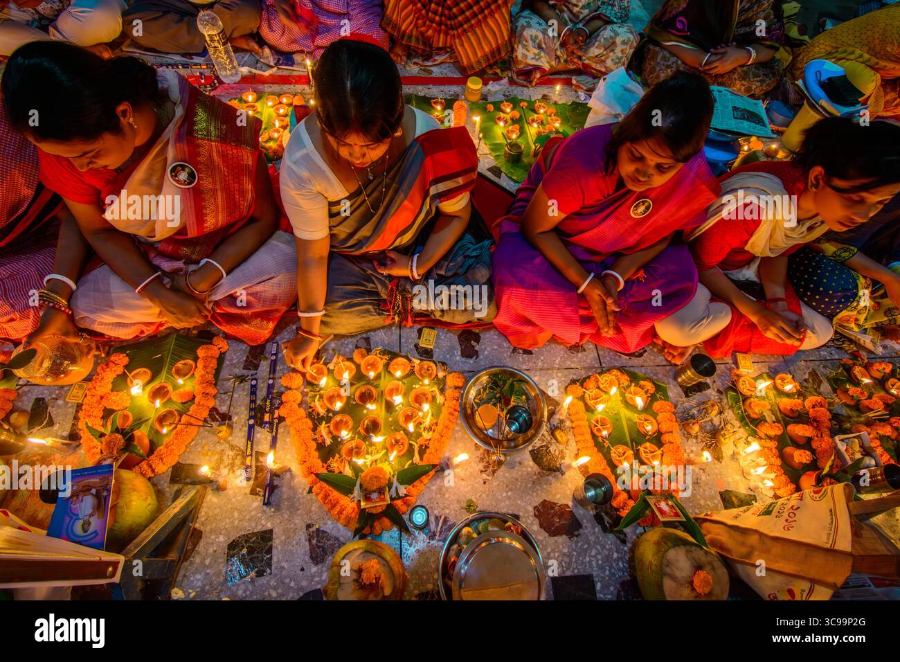 Dhaka, Bangladesh - 13 novembre 2018 : vue de femmes dans des saris colorés, têtes inclinées dans la prière, au milieu de la douce lueur des bougies et des soucis vibrants. Banque D'Images