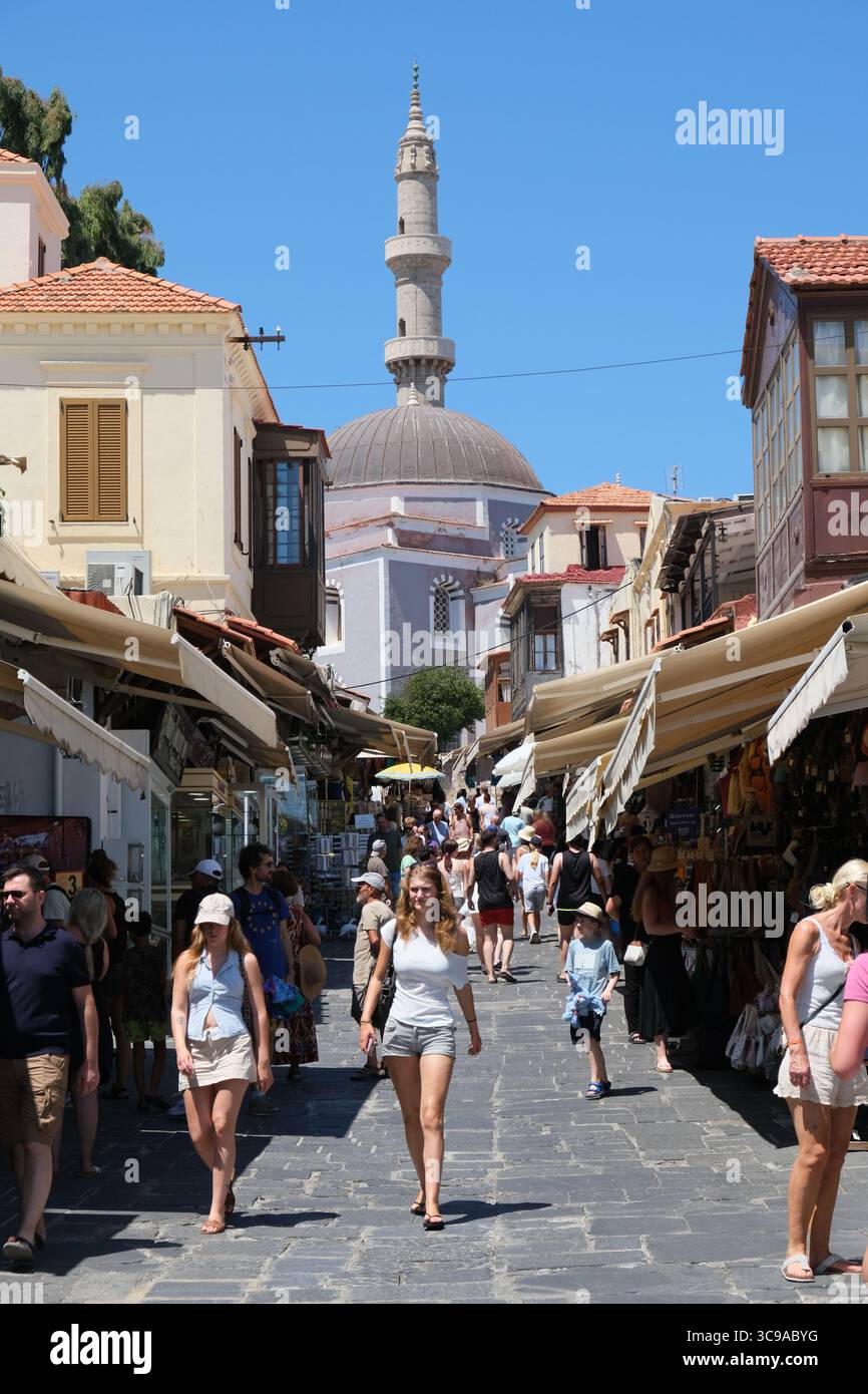 Les touristes descendent la rue Socrates dans la vieille ville de Rhodes, un site classé au patrimoine mondial de l'UNESCO, avec la mosquée Suleiman en arrière-plan Banque D'Images