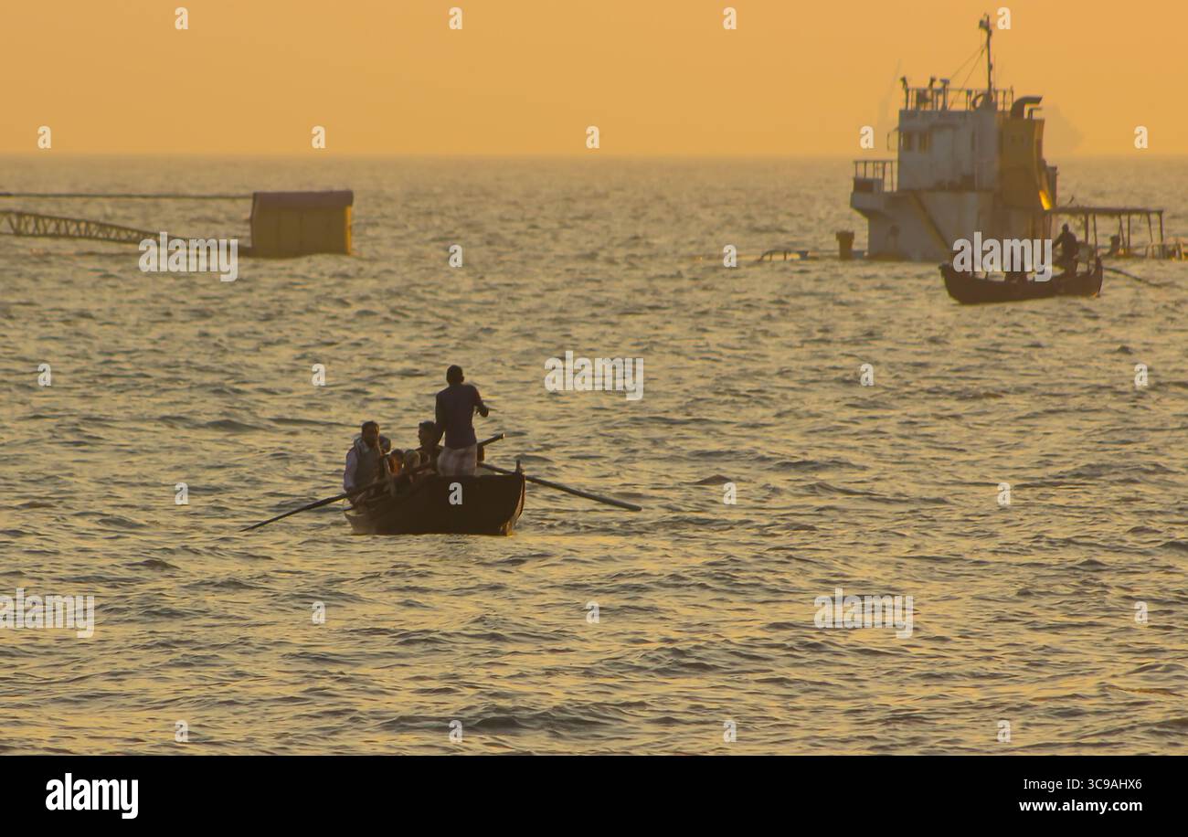 Chittagong, Bangladesh - 02 novembre 2018 : vue de bateaux silhouettes glissant dans les eaux dorées, avec une structure partiellement submergée ajoutant un contraste mystérieux au paysage marin serein. Banque D'Images