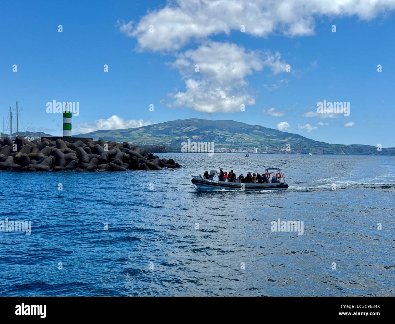 Bateau rapide touristique de retour à la marina de Ponta Delgada après un voyage de plongée, avec la montagne volcanique de Lagoa do Fogo en arrière-plan, São Miguel Isl - Image de stock capturée avec un smartphone