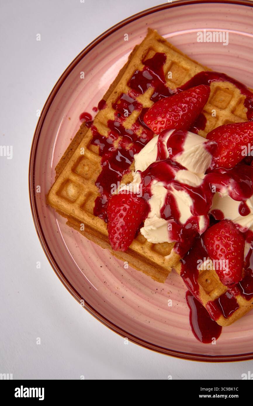 Gaufres délicieusement confectionnées avec fraises fraîches et garniture crémeuse arrosée de sauce sucrée, parfait pour toute occasion gourmande Banque D'Images