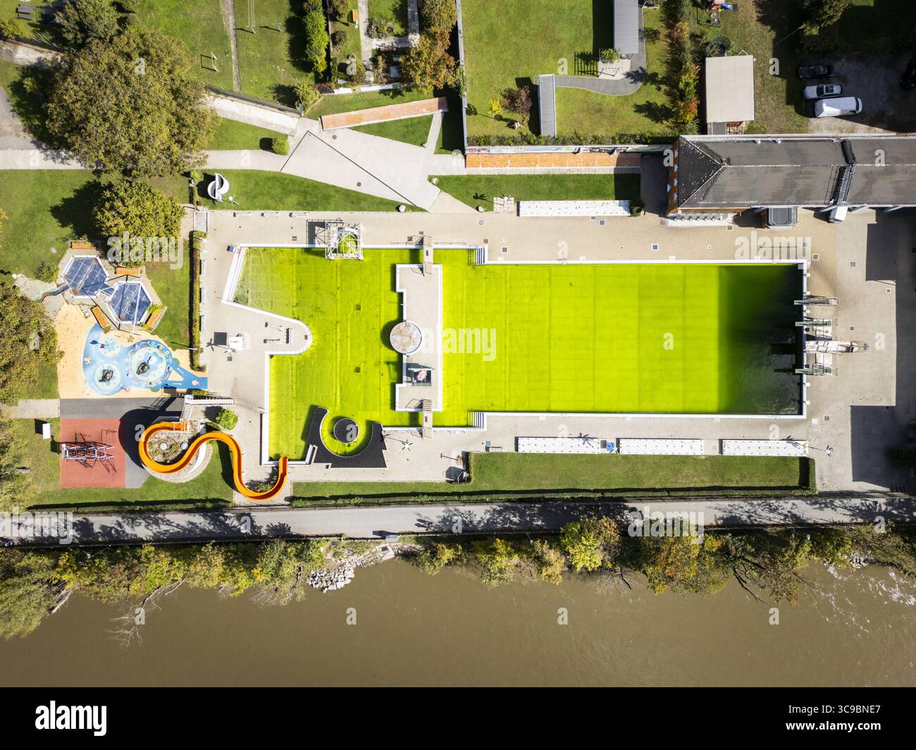 Vue aérienne d'un complexe de piscines verdoyantes contrastant avec les tons terreux du paysage environnant et de la rivière, Graz, Styrie, Autriche. Banque D'Images
