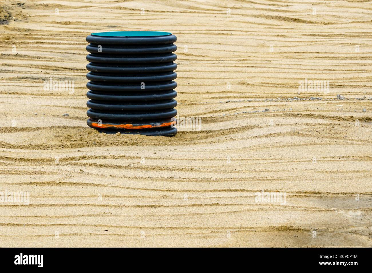 Une chambre d'inspection en plastique ondulé noir dépasse d'un chantier de construction compacté par du sable pendant le travail du sol Banque D'Images