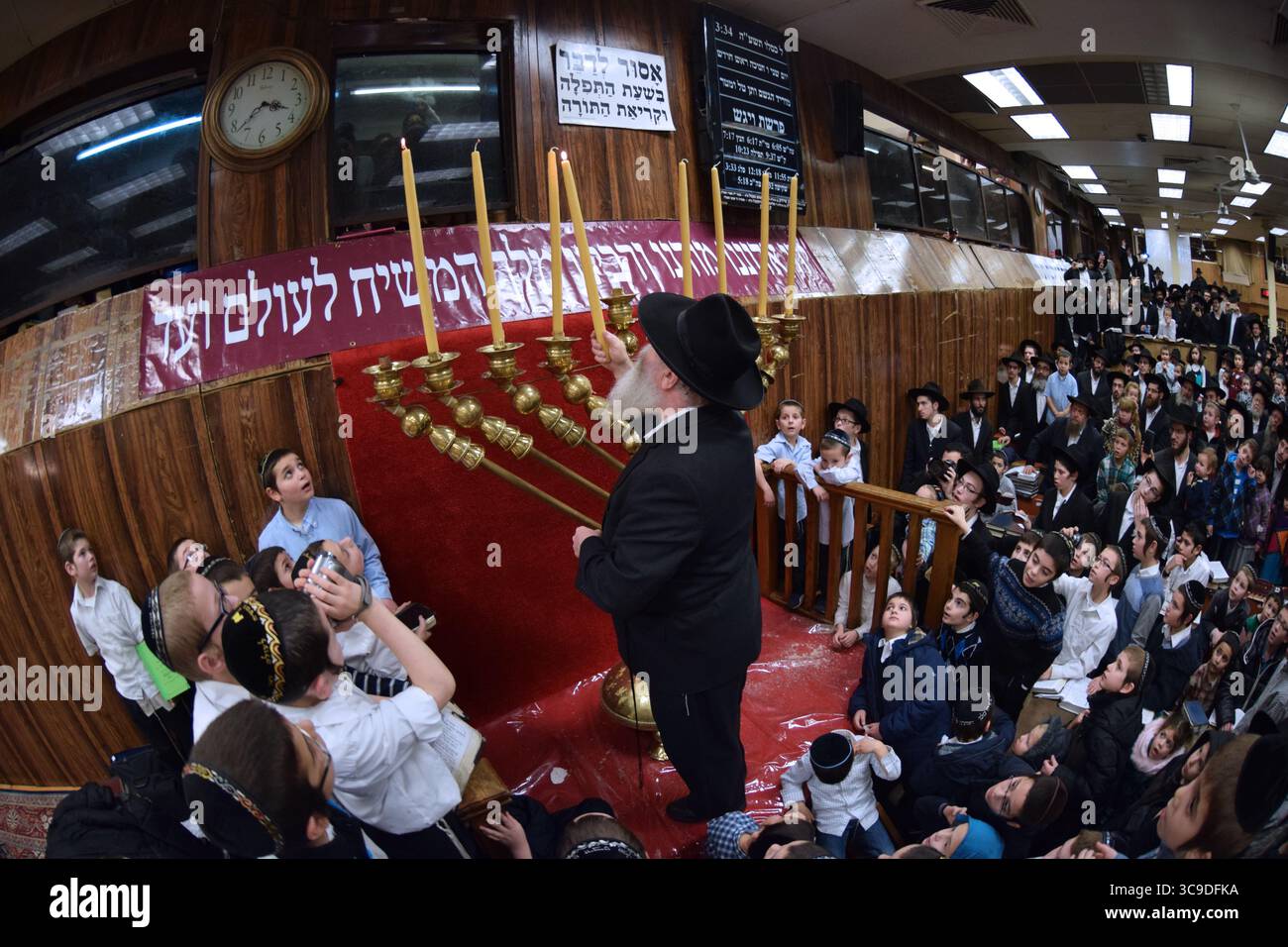 Un rabbin juif orthodoxe récite des bénédictions avant d'allumer des bougies Hanukkah dans une synagogue bondée à Crown Heights, Brooklyn, New York Banque D'Images