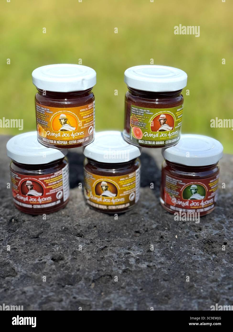 Cinq pots de produits alimentaires traditionnels des Açores exposés à l'extérieur sur une surface en pierre avec de l'herbe en arrière-plan. - Image de stock capturée avec un smartphone