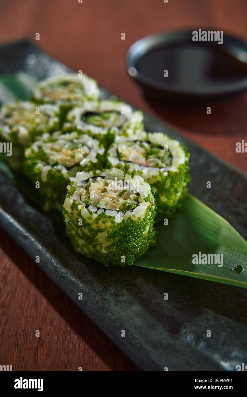 Un gros plan de petits pains de Sushi vert fraîchement arrangés sur une élégante assiette noire, accompagné d'un petit plat de sauce soja, parfait pour un pré culinaire Banque D'Images