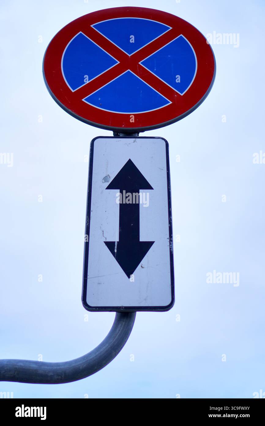 Panneau indiquant l'interdiction de stationnement sur le bord de la route et montrant une croix rouge et deux flèches verticales pour l'application des directives. Banque D'Images