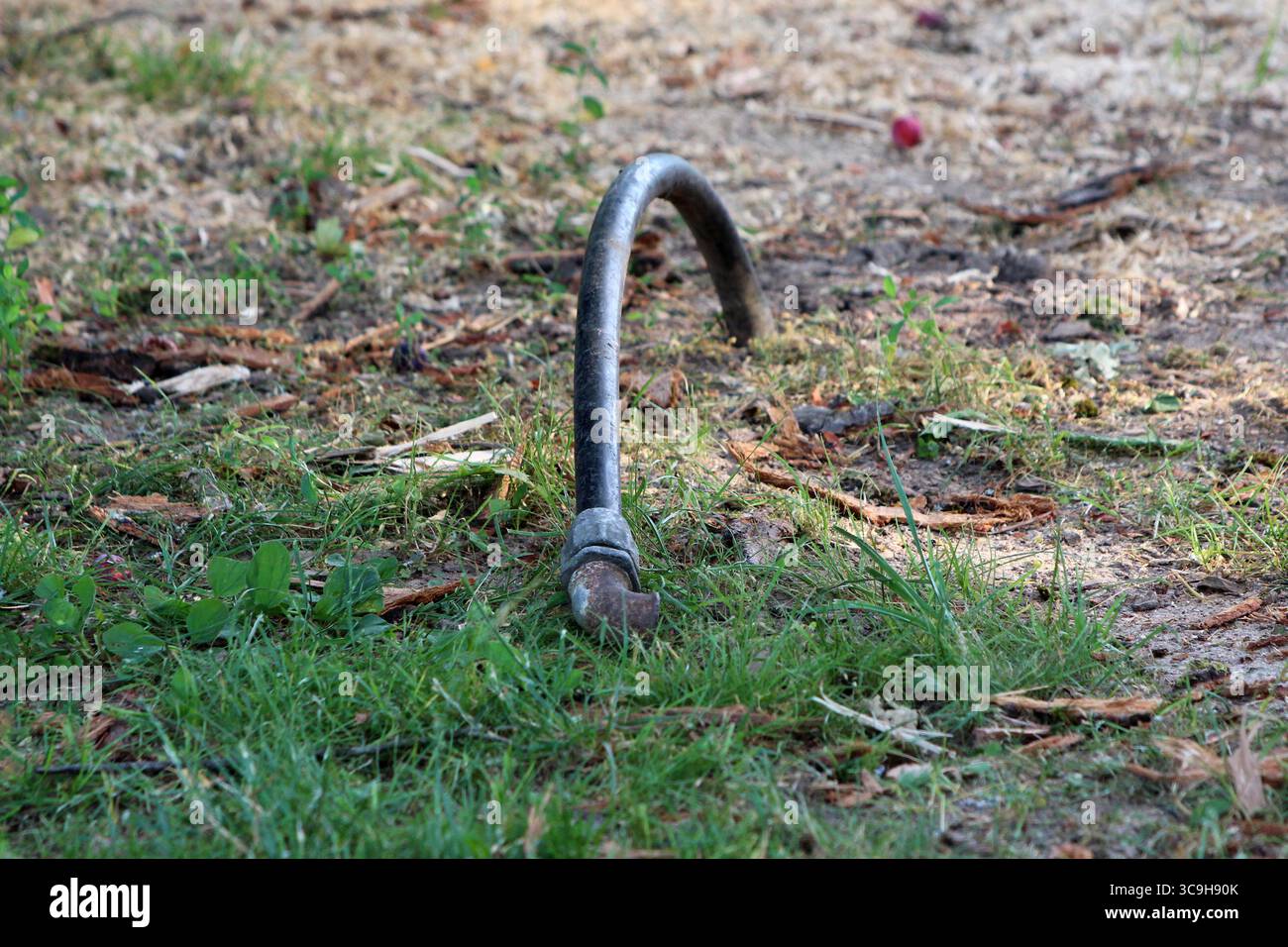 Un tuyau métallique courbé émerge de la terre au milieu de l'herbe et des débris de bois dispersés, marquant peut-être un ancien service public ou un point d'ancrage dans un parc public Banque D'Images Un tuyau métallique courbé émerge de la terre au milieu de l'herbe et des débris de bois dispersés, marquant peut-être un ancien service public ou un point d'ancrage dans un parc public Banque D'Images