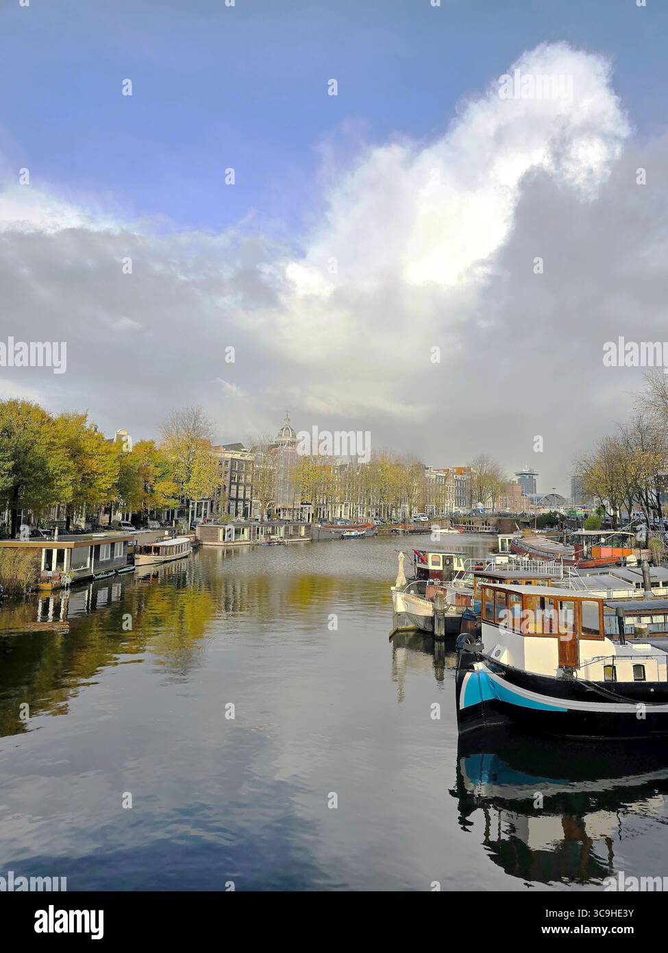 Des bateaux et des arbres d'automne bordent un canal calme à Amsterdam sous un ciel spectaculaire, capturé près d'un pont classique. - Image de stock capturée avec un smartphone