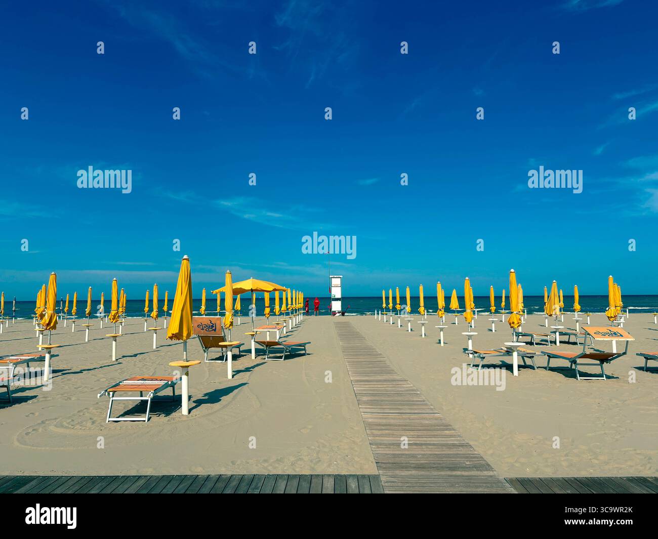 Chaises longues avec parasols jaunes sur la plage de sable. Parapluies fermés et chaises longues vides par temps venteux. Concept de vacances. Banque D'Images