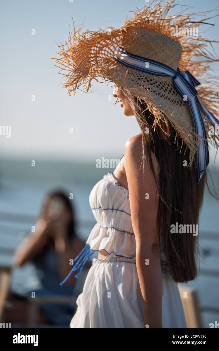 Femme avec les cheveux longs bruns et chapeau de paille en robe d'été marchant près d'un lac Banque D'Images