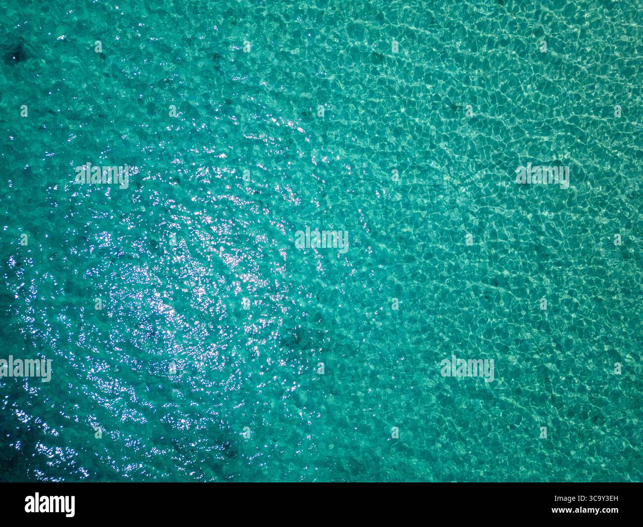 Vue aérienne de la mer turquoise scintillante avec des rochers sous-marins visibles à travers l'eau claire. Surface paisible reflétant la lumière du soleil lors d'une journée d'été calme Banque D'Images