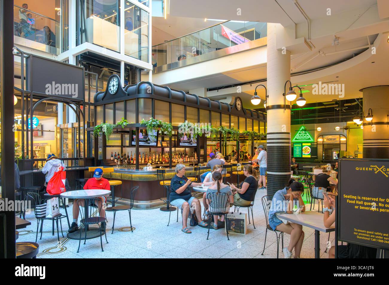 Les gens s'assoient et discutent autour d'un bar central sous des plantes suspendues et des écrans de télévision dans une salle de restauration intérieure lumineuse dans le Centre Eaton. Banque D'Images