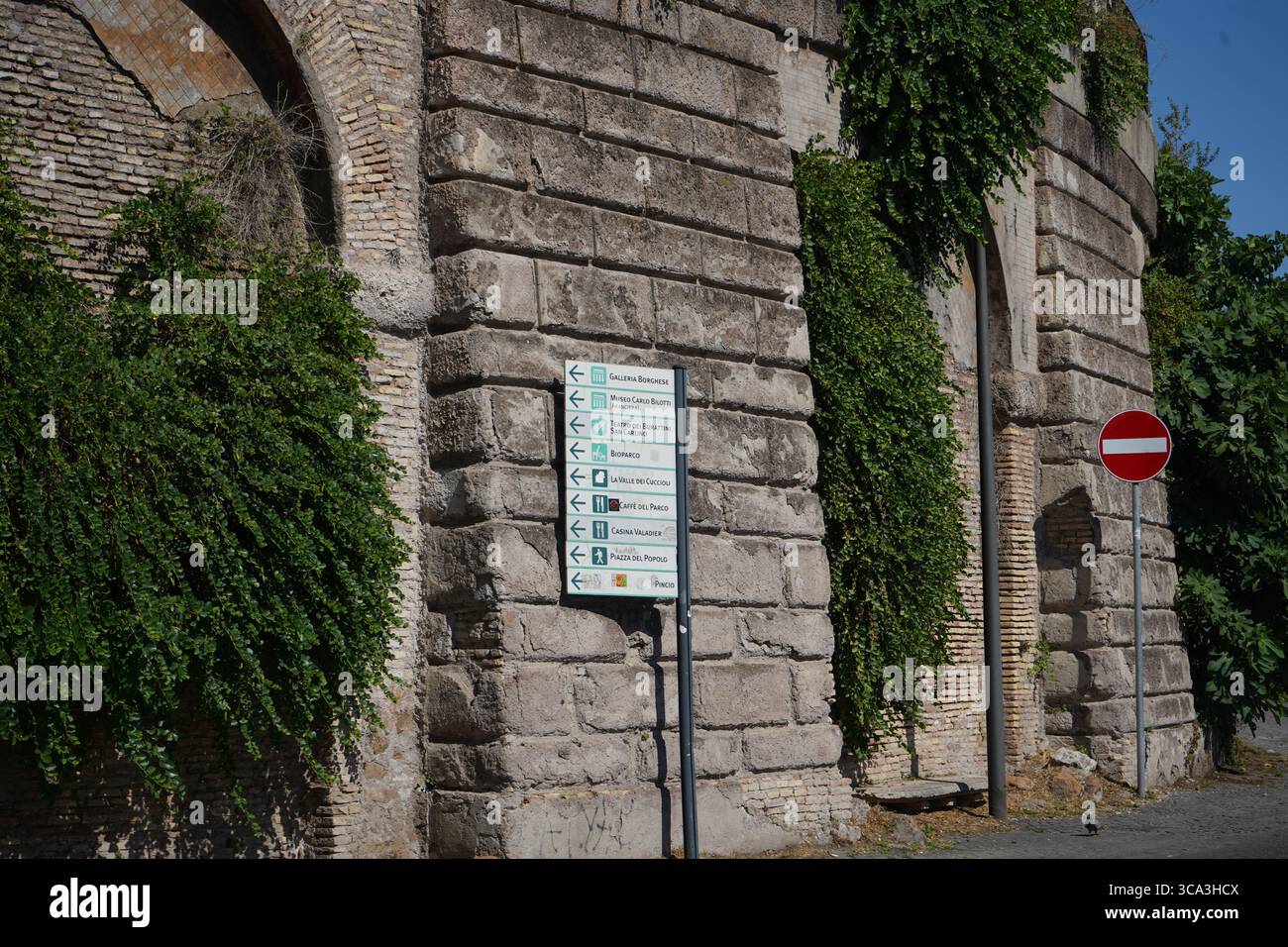 Navigation dans l'histoire : un panneau directionnel guide les visiteurs le long d'un ancien mur de pierre recouvert de lierre à Rome, en Italie, évoquant un sentiment de voyage intemporel. Banque D'Images