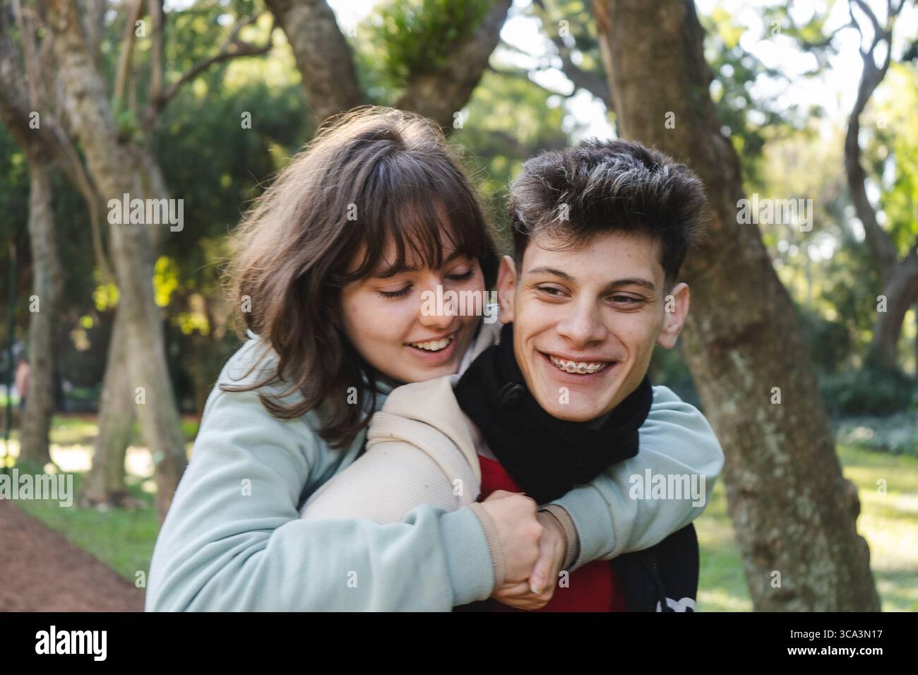Adolescente donnant piggyback ride à adolescent souriant dans un parc, exprimant l'amour et le bonheur de la jeunesse Banque D'Images