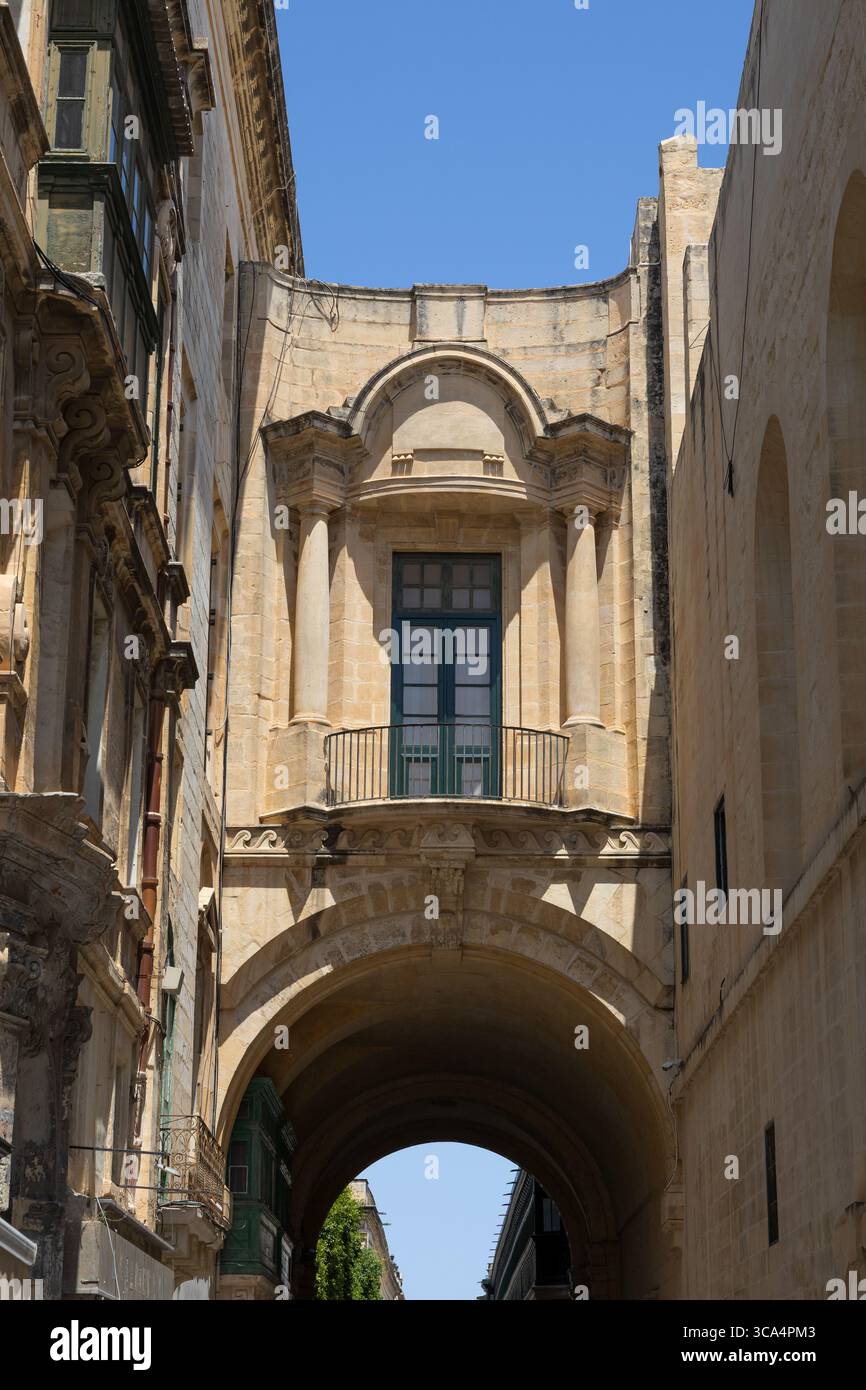 Old Theatre Street, avec la passerelle fermée voûtée et balcon à la Bibliothèque nationale, la Valette, Malte. Banque D'Images
