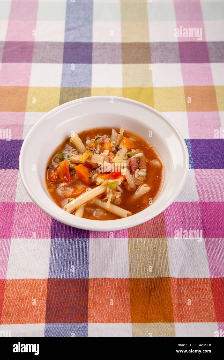 bol de soupe minestrone copieux, débordant de légumes vibrants et de pâtes, repose sur une nappe joyeuse à carreaux Banque D'Images