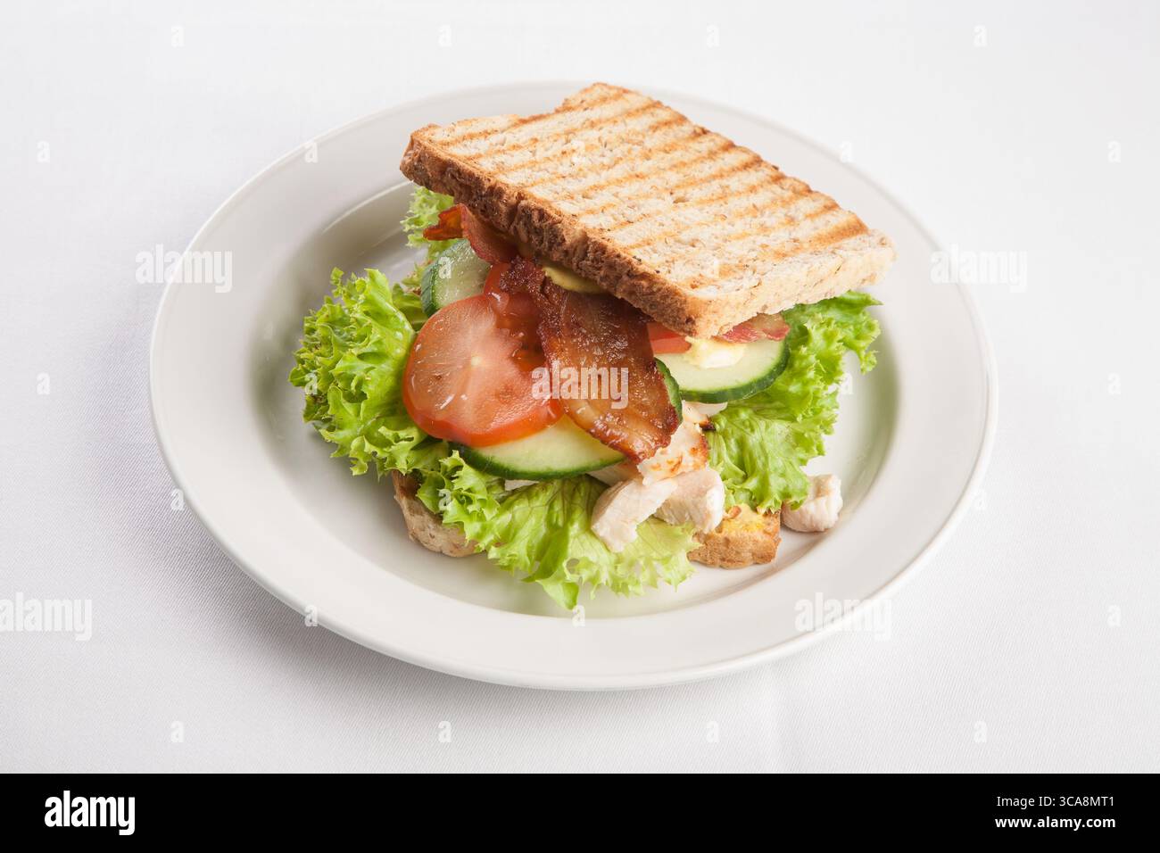 Sandwich grillé sur une assiette blanche remplie de salade, bacon, concombre et poulet, un repas classique et appétissant, shot de nourriture de studio Banque D'Images