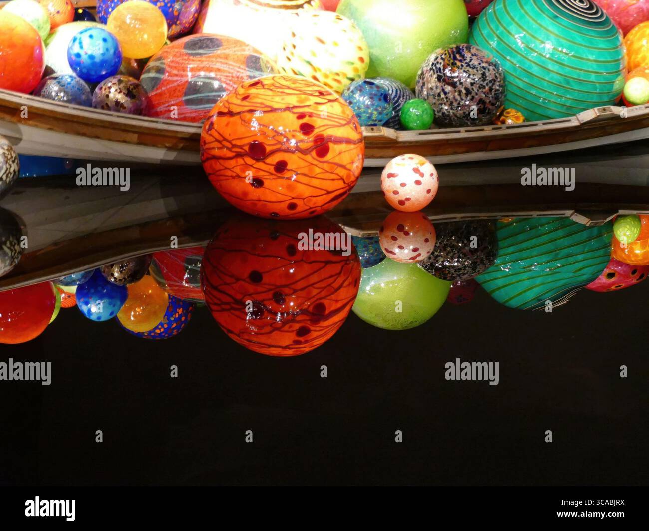 SEATTLE - APR 25, 2025 - sphères de verre colorées de différentes tailles et motifs reposant dans un conteneur en forme de bateau, reflétant la lumière vibrante dans l'obscurité Banque D'Images