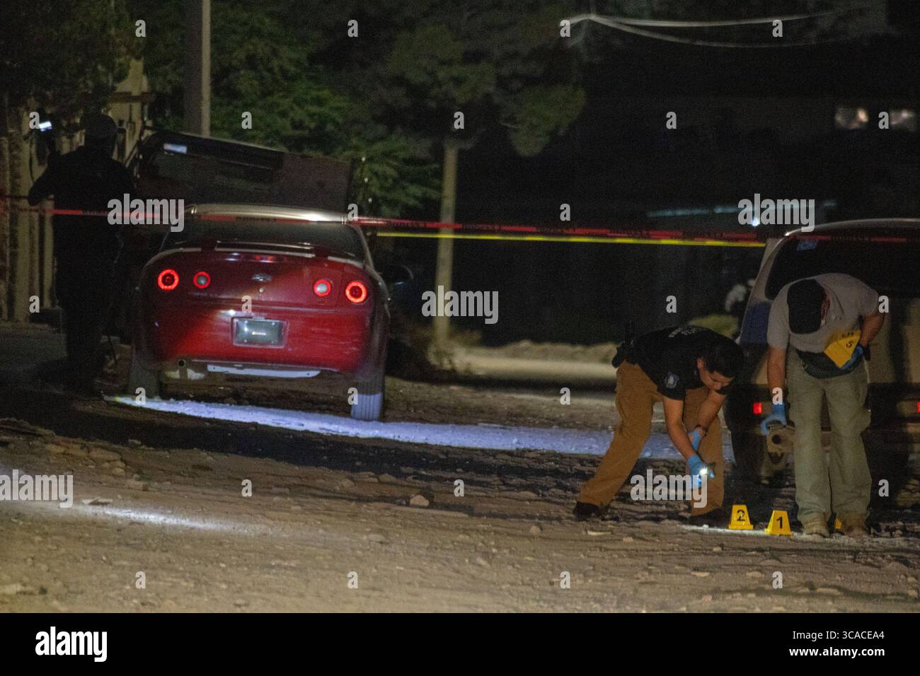 L'équipe médico-légale sonde la scène de crime nocturne près d'une voiture rouge à Ciudad Juarez, victime de violence. Banque D'Images