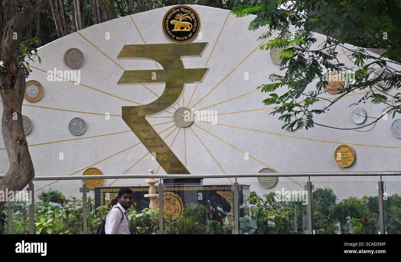 Un homme passe devant une installation de symboles de roupies devant le bâtiment de la Reserve Bank of India (RBI) à Mumbai. Le symbole de la roupie est la monnaie officielle de l'Inde utilisée dans toutes les transactions financières de biens et services à travers le pays. Banque D'Images